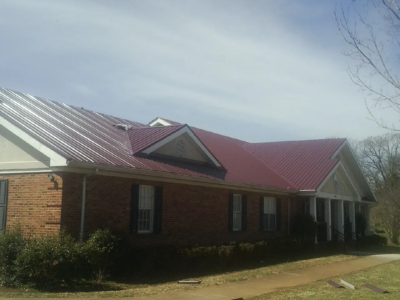 Red metal roof with gabled entries on a long brick building, from a Hail Damage Roof Repair job in Ross
