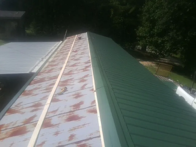 Old rusted panels beside newly installed green metal roofing — Wind Damage Roof Repair by Roofing Brothers in Ross