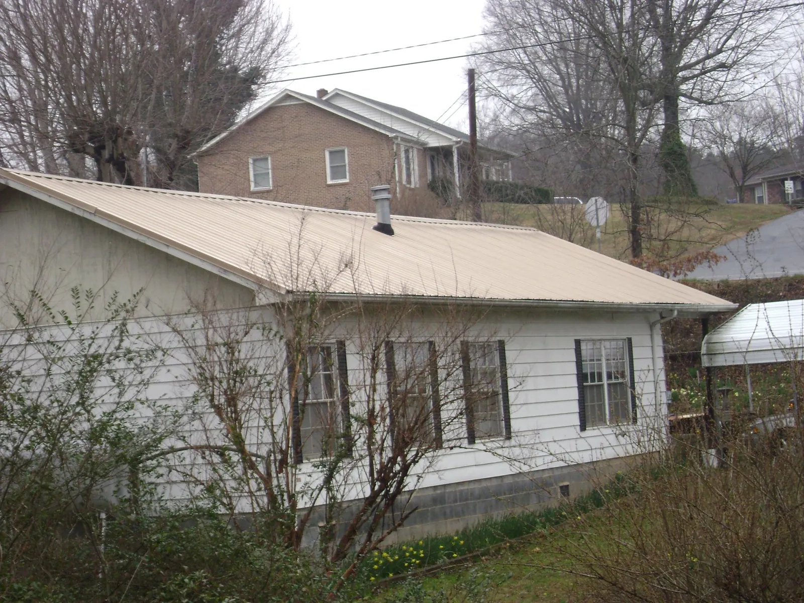 Tan metal roof on a white sided house set into a hillside — Commercial Roofing by Roofing Brothers in Ross
